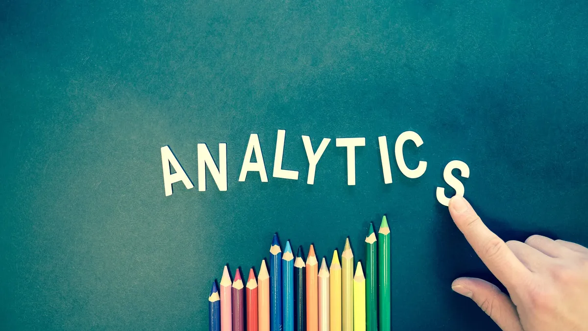 The word “Analytics” spelled out on a table by a hand in wooden letters.