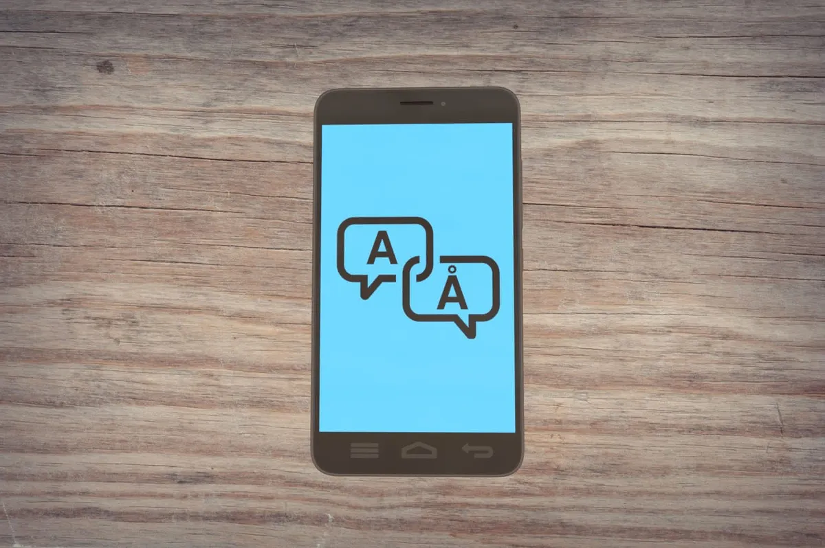An Android smartphone resting on a table showing two chat bubbles: one with an “A” character and the other “Å” (a-ring) character.