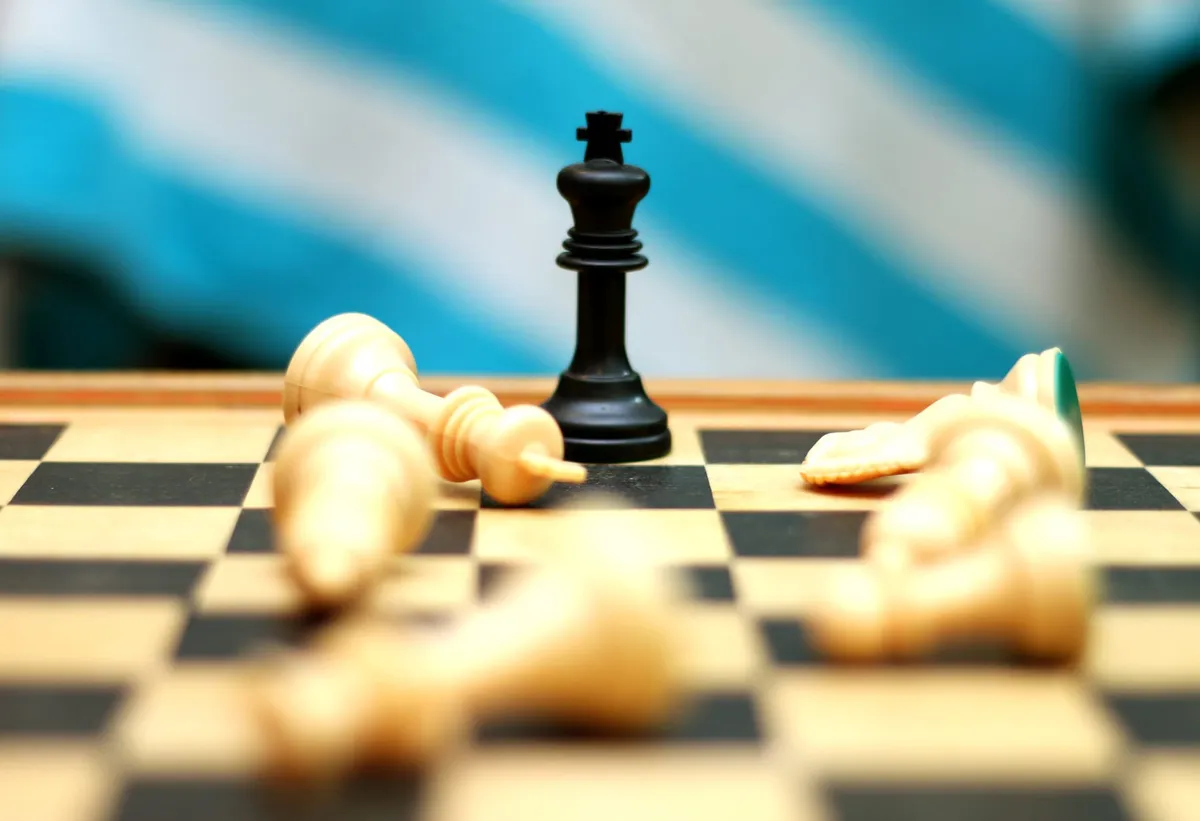 A black king chess piece wins the match with white pieces scattered around it as a battle field.