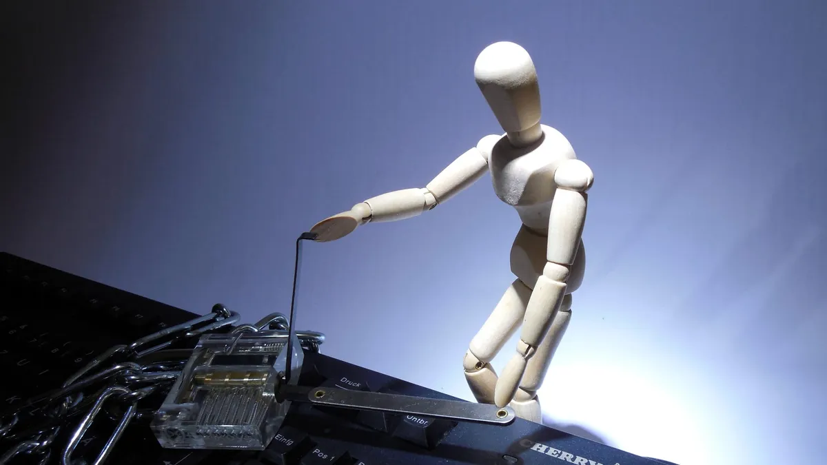 A mini mannequin lockpicking a dummy padlock on top of a computer keyboard.