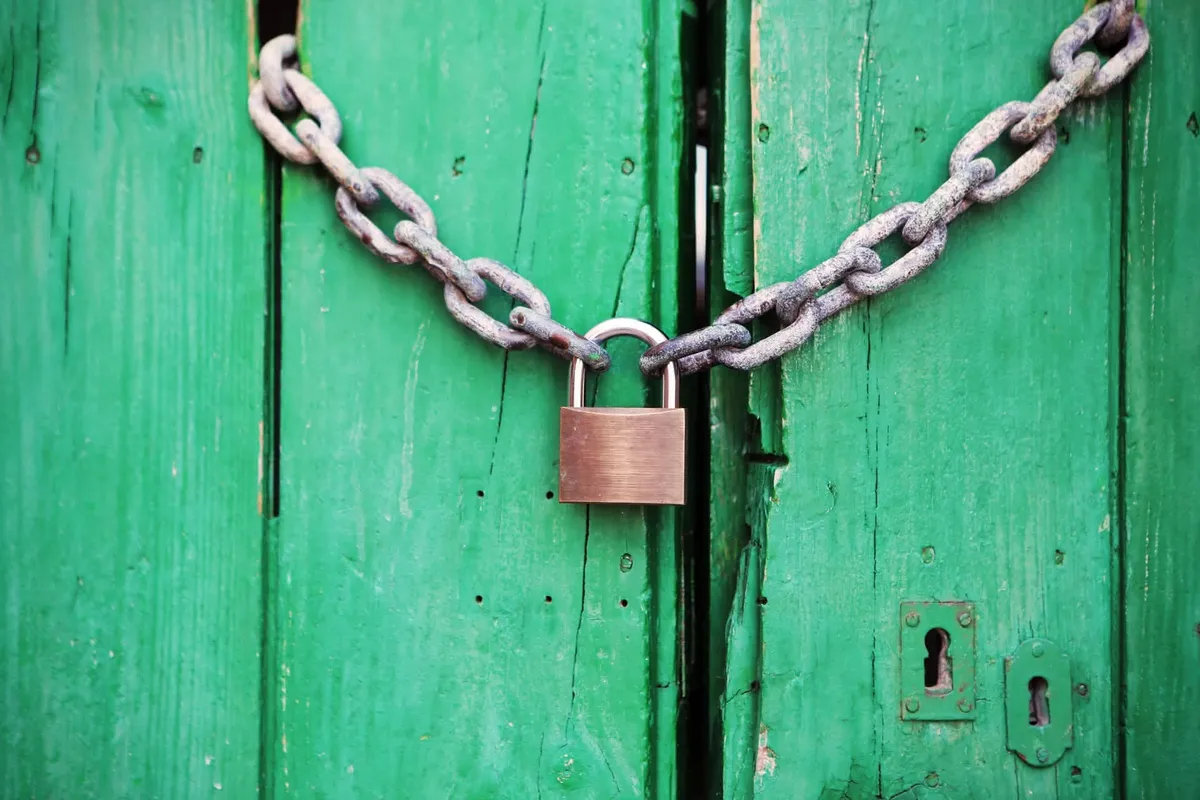 An old green door closed behind a padlock and chain.