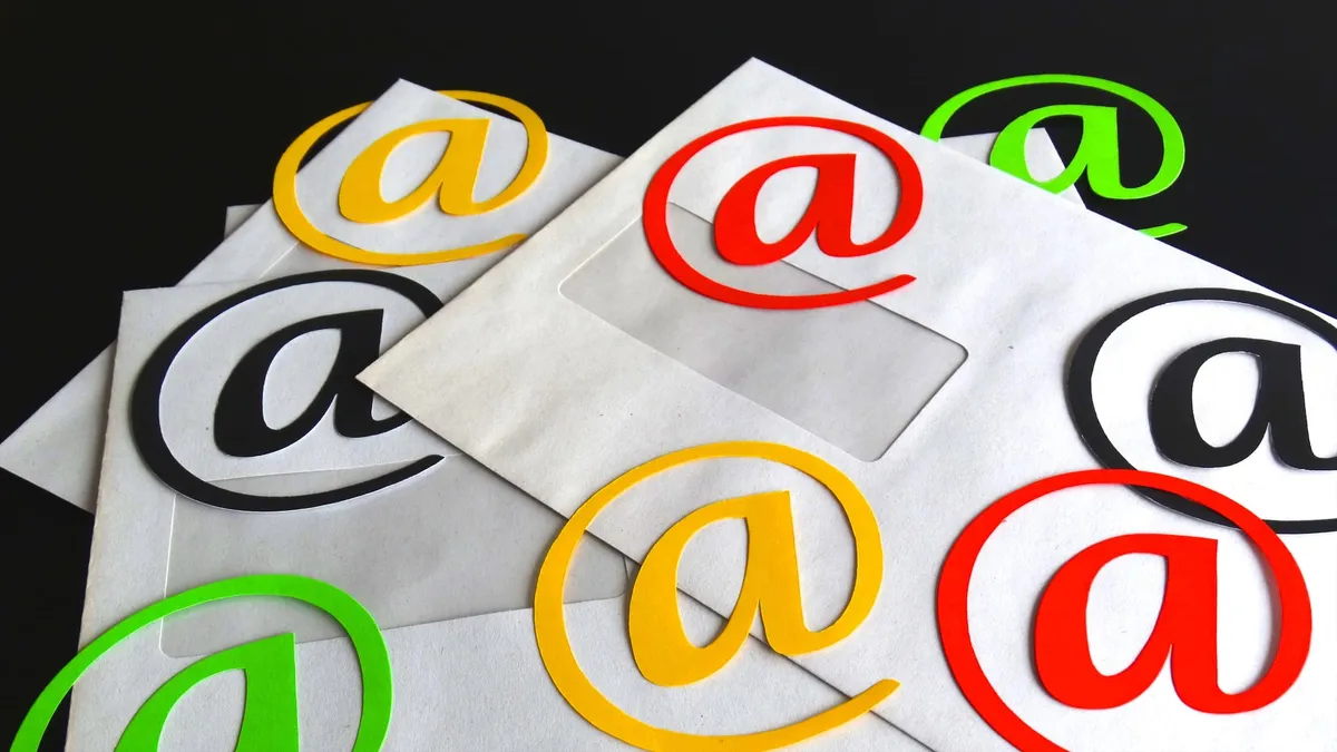 Envelopes with a cut-out and  colored “@” symbols laying on top of them.