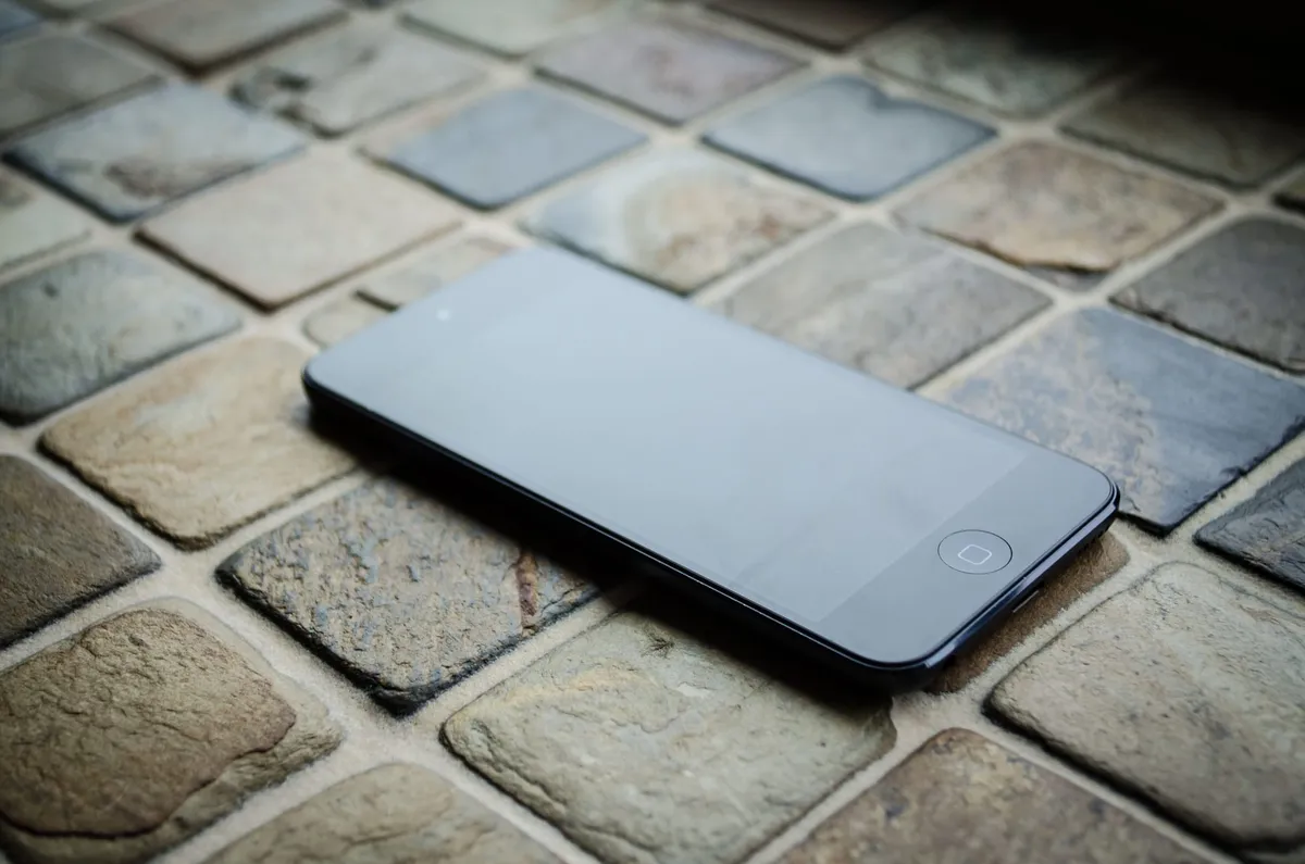 An iPod Touch lying on a brick floor.