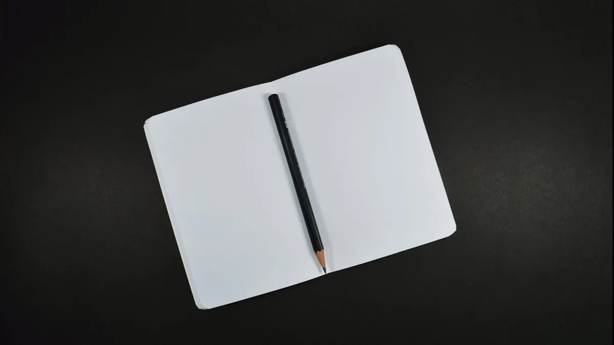 An empty white journal pen and black pencil against a black table.