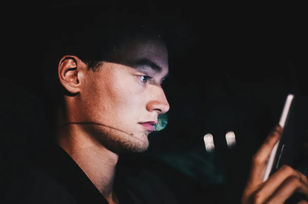 A man sits in the dark looking into his smartphone.