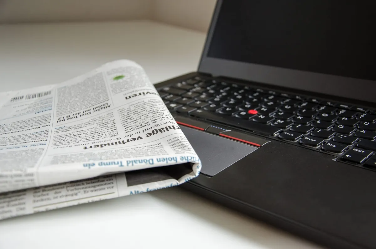 A folded newspaper lays on top of a laptop computer with a switched-off display.