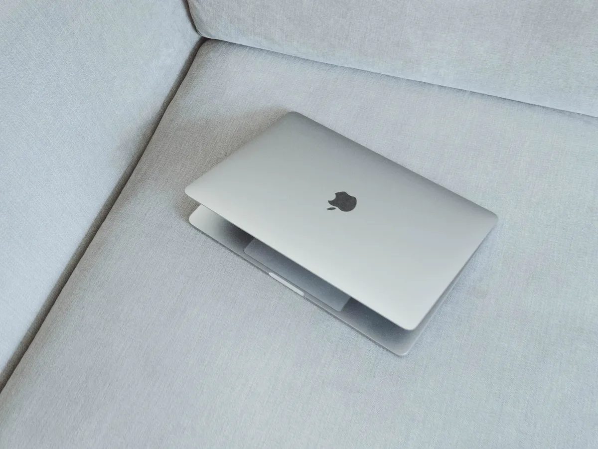 A half-closed MacBook laptop computer laying in a gray sofa.