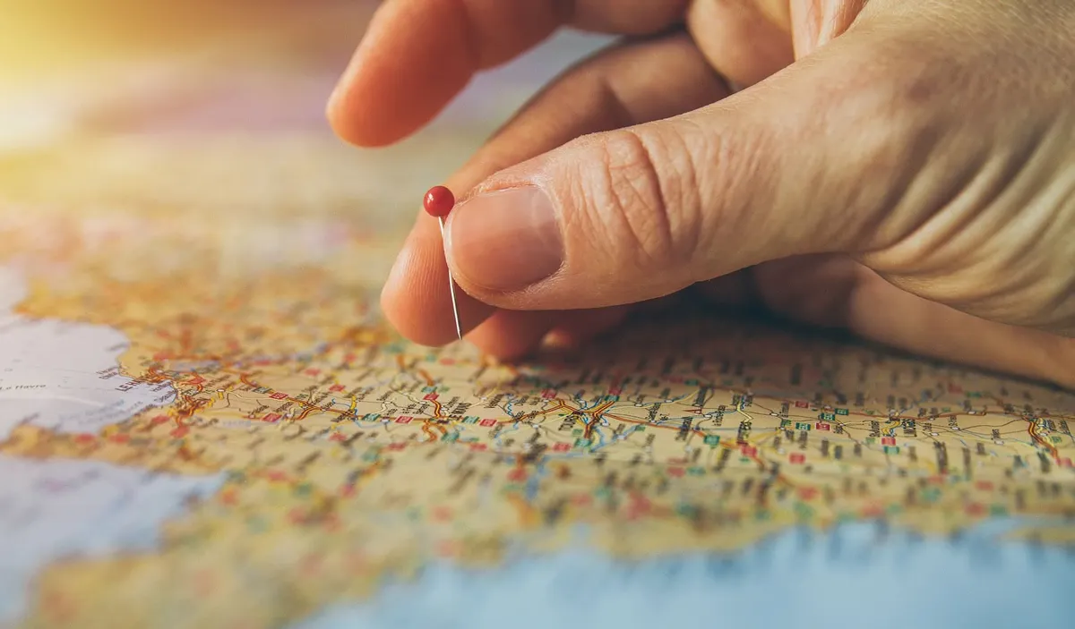 A hand placing a pin on a map.