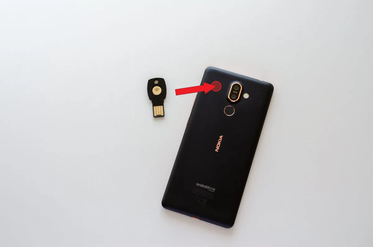 The backside of a Nokia 7 Plus smartphone with an arrow pointing from a blue NFC security key device and onto the left side of the camera on the smartphone.
