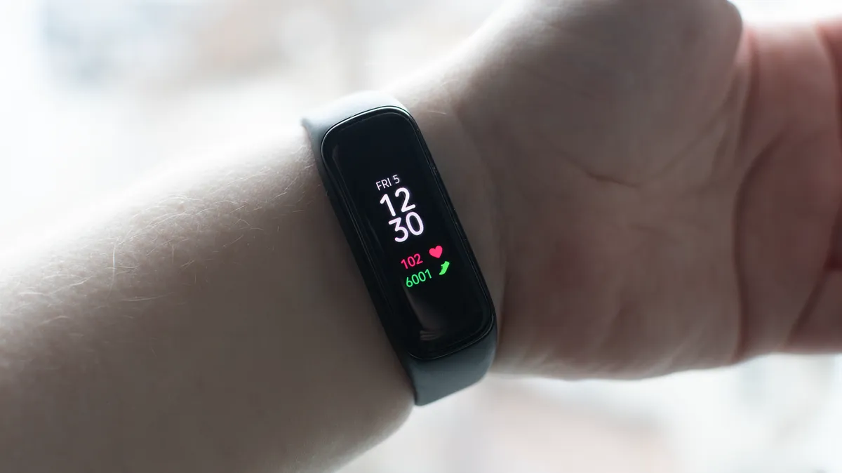 An outstretched arm showing off a Samsung Galaxy Fit2 activity armband. The armband is small with a bright display showing the current time, heart rate, and step count.