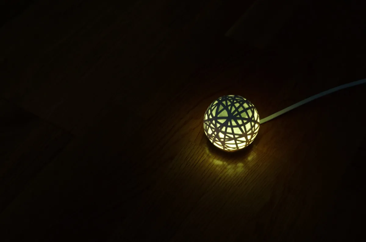 A green glowing Sense sleep monitoring device sitting on a wooden table in the dark.