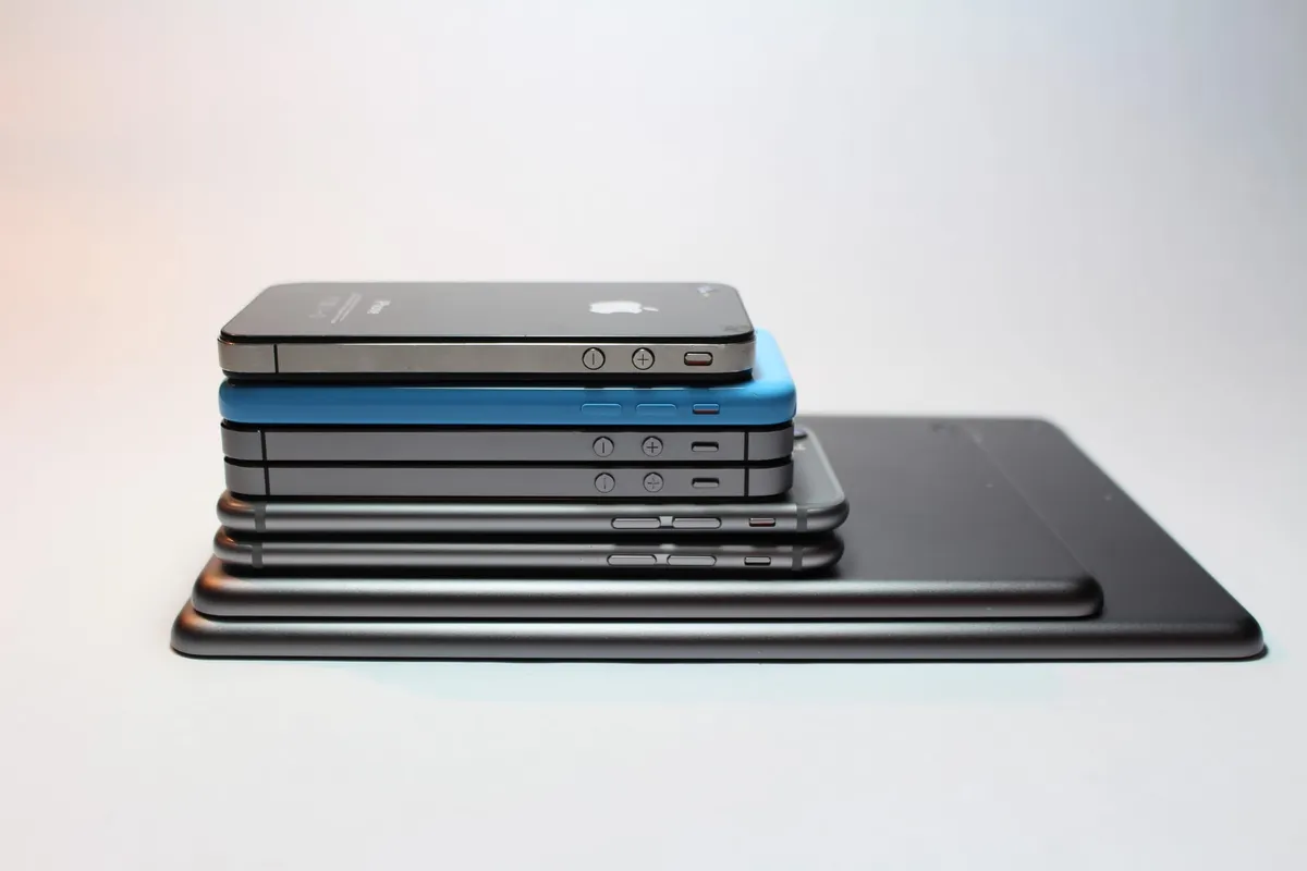 Eight different iPods, iPads, and iPhones stacked on top of each other.