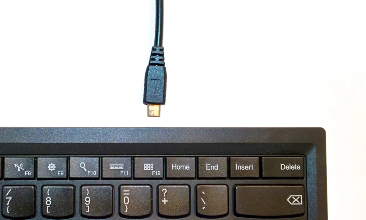 A computer keyboard with a loose Micro-USB cable pointed at it.
