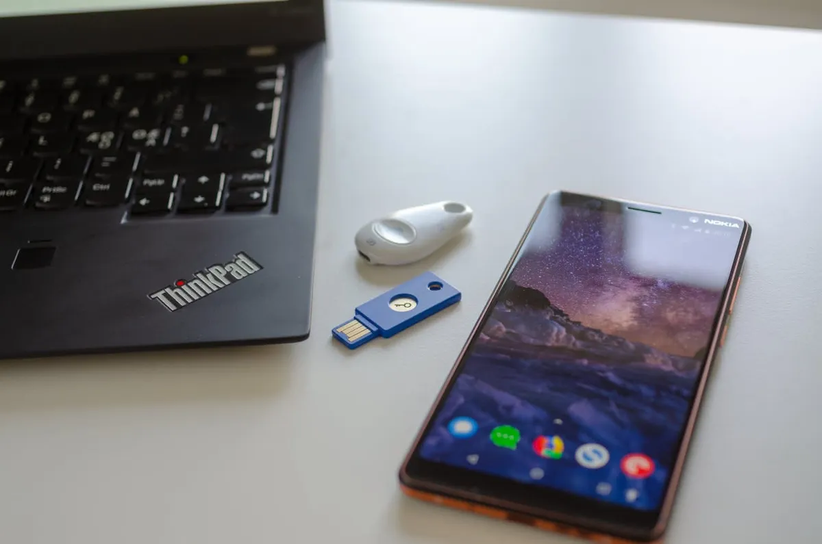 Two different U2F security key devices placed on a table between a ThinkPad laptop and a Nokia smartphone.