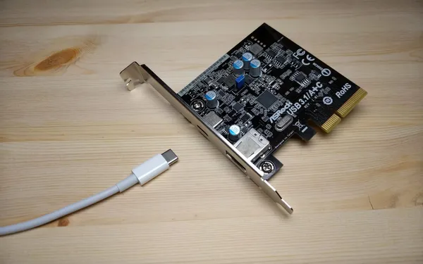 A PCIe card with one USB Type-A and a Type-C port laying on a wooden table. A white Type-C cable runs up to but isn’t connected to the Type-C port.