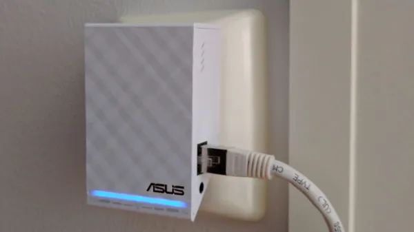 An ASUS RP-AC52 Wi-Fi repeater plugged into a wall outlet with an Ethernet cable connected.