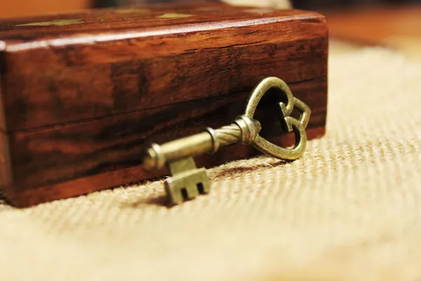 An old brass key resting in front of a wooden box on a table.