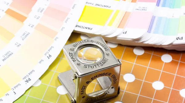 A magnifying glass placed next to a color palette and thread counters.