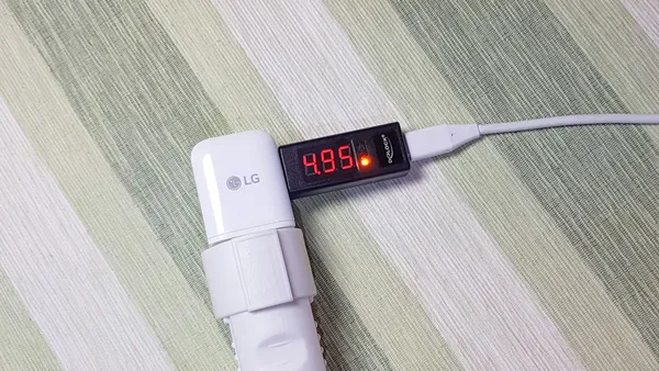 An LG-branded USB charger connected to an outlet. A USB ammeter is connected to the charger and showing 4,95 volt from a connected USB Type-C cable.