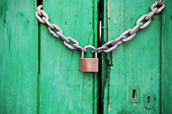 An old green door closed behind a padlock and chain.