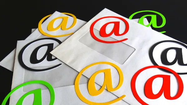 Envelopes with a cut-out and  colored “@” symbols laying on top of them.