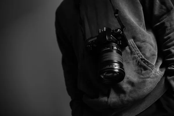 A camera hanging from a strop around the next of a person wearing a hoodie.
