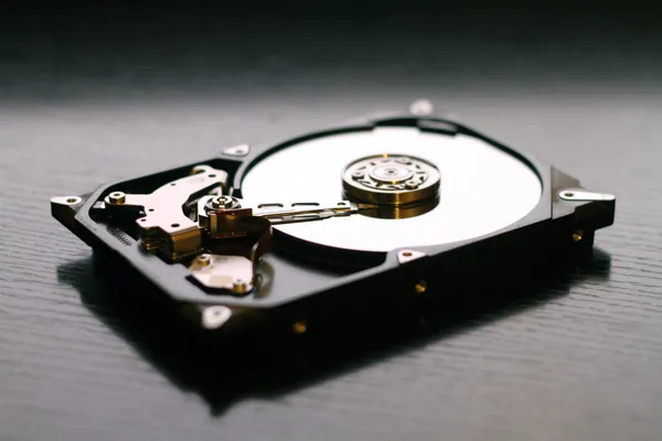 An open hard drive resting on a table exposing the internal disk and read head.