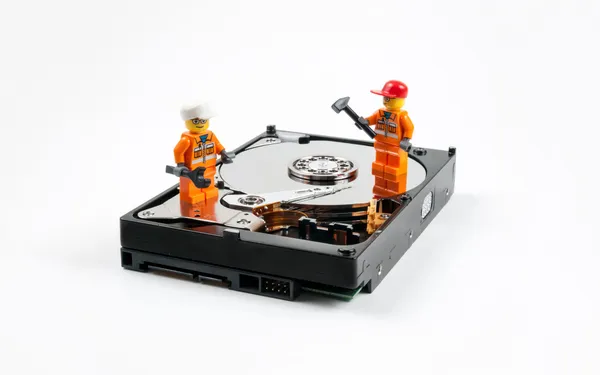 Two Lego brick figure construction workers stands on top of a hard drive with the hard disk drive platter exposed.