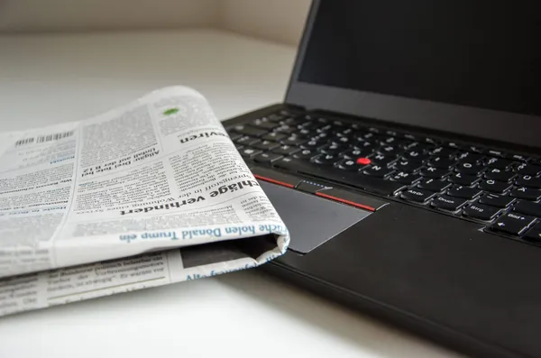 A folded newspaper lays on top of a laptop computer with a switched-off display.
