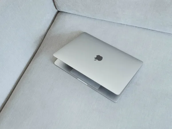 A half-closed MacBook laptop computer laying in a gray sofa.