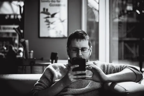 A man sitting on a couch while reading on his phone.