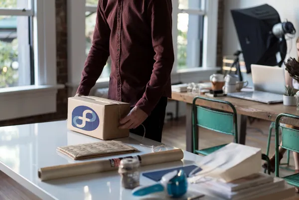 A man ties a box with the Feodra Linux logo on the front in an office.