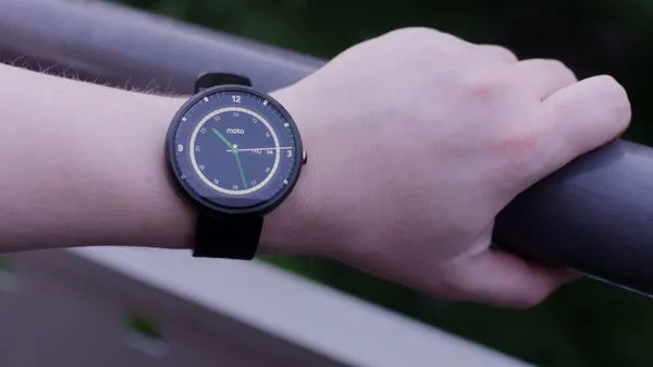 A Moto 360 smartwatch with a lit display worn on a wrist.