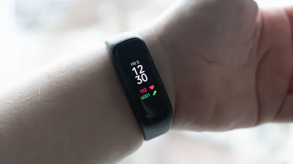 An outstretched arm showing off a Samsung Galaxy Fit2 activity armband. The armband is small with a bright display showing the current time, heart rate, and step count.