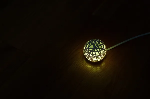 A green glowing Sense sleep monitoring device sitting on a wooden table in the dark.