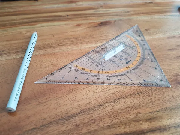 A triangular ruler and gray pencil on a wooden surface.