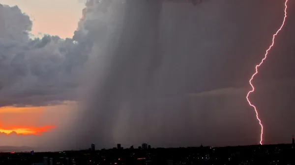 A lightning bolt strikes the ground in the distance during a rainy thunderstorm.