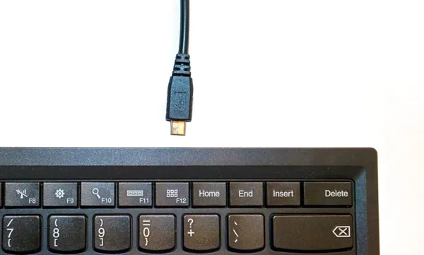 A computer keyboard with a loose Micro-USB cable pointed at it.