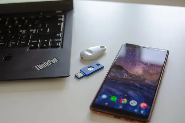 Two different U2F security key devices placed on a table between a ThinkPad laptop and a Nokia smartphone.