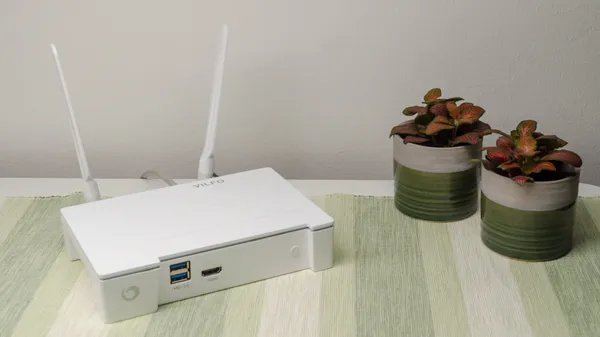 The Vilfo wireless VPN router resting on a table next to two potted plants.
