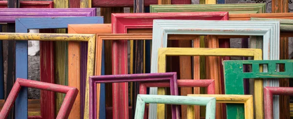 A large stack of worn old window frames in different colors.