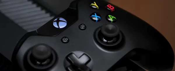 A close-up of an Xbox One Controller sitting on top of an Xbox One.
