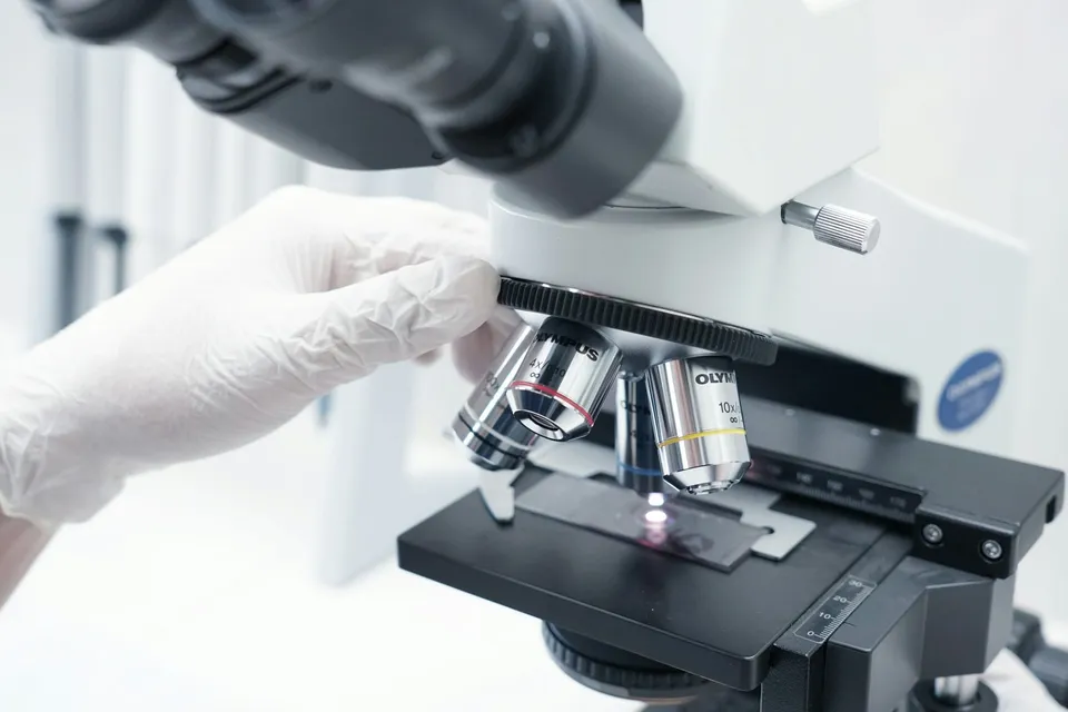 Scientist wearing gloves examining a sample through a microscope in a lab.
