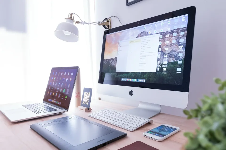 Minimal workspace with an iMac and iPhone on a wooden desk in soft natural light.