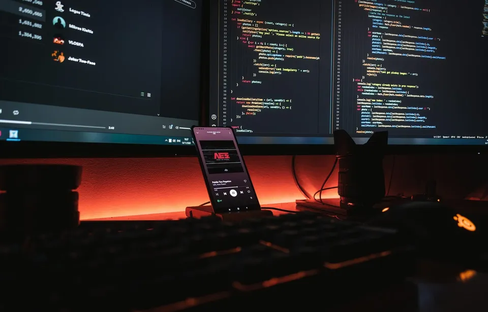 Desk setup with dual monitors showing source code and a smartphone, representing a software development environment.