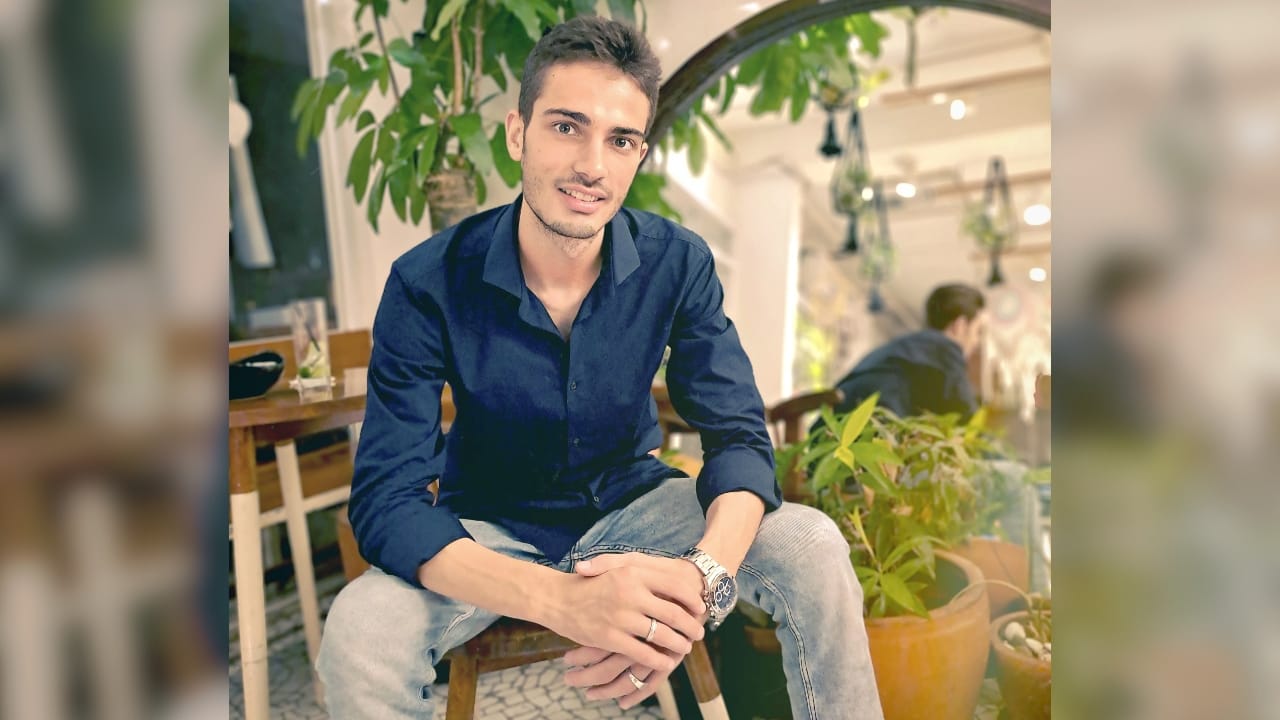 A portrait photo of Sayid Bilal sitting on a chair, surrounded by plants.