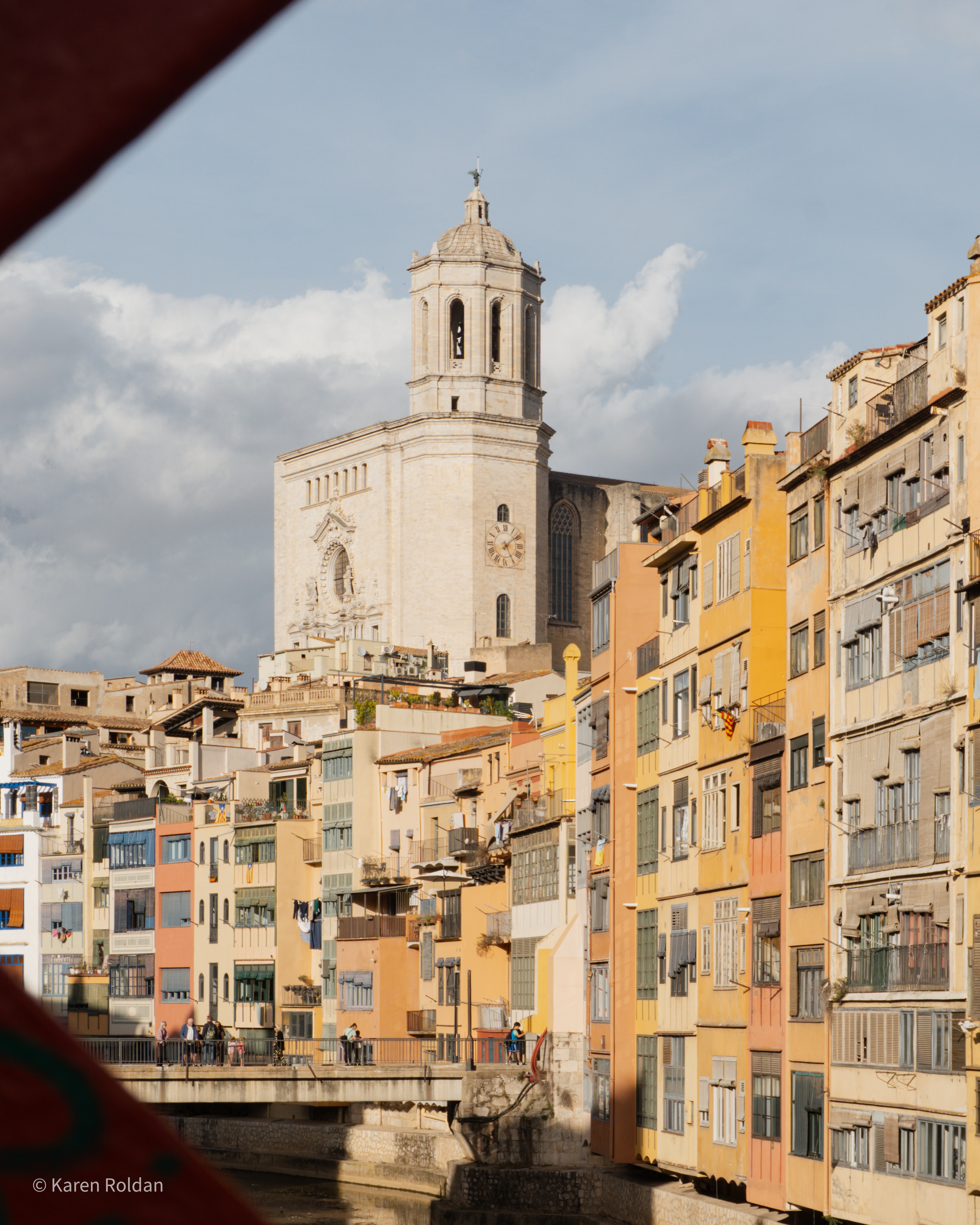 Colorful houses along the Onyar River with the Girona Cathedral tower rising in the background.