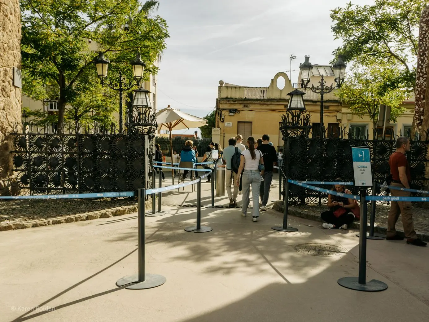 The exit area of Park Güell featuring ornate wrought iron gates and a blue 'Sortida' exit sign.