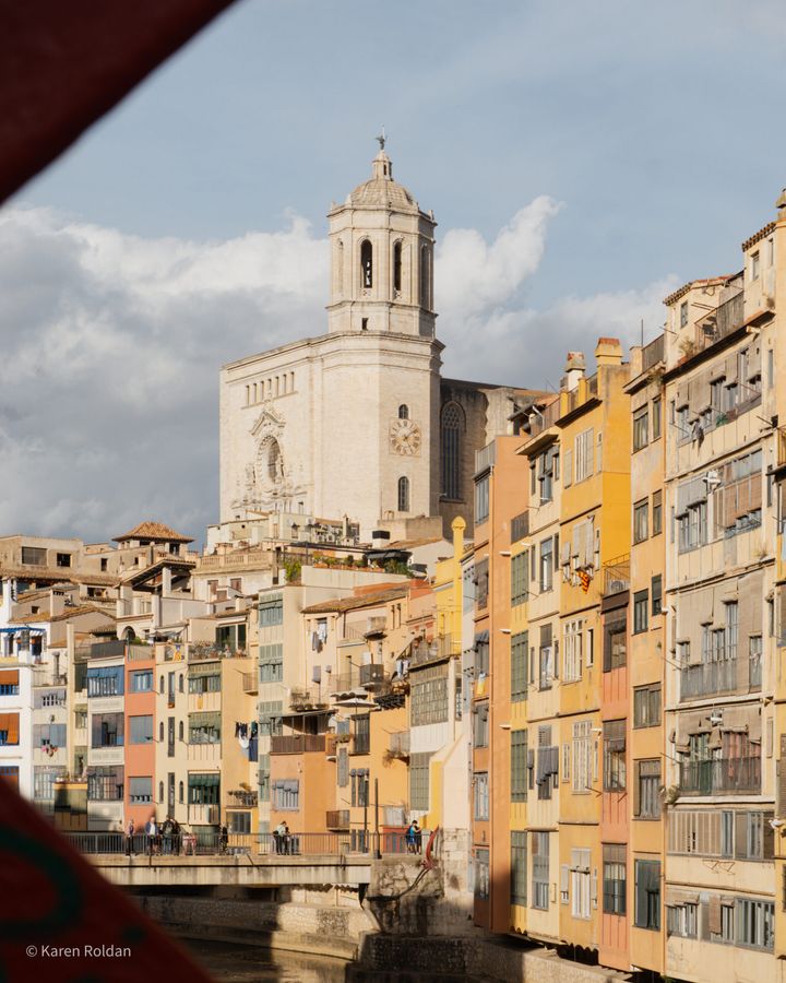 Colorful houses along the Onyar River with the Girona Cathedral tower rising in the background.