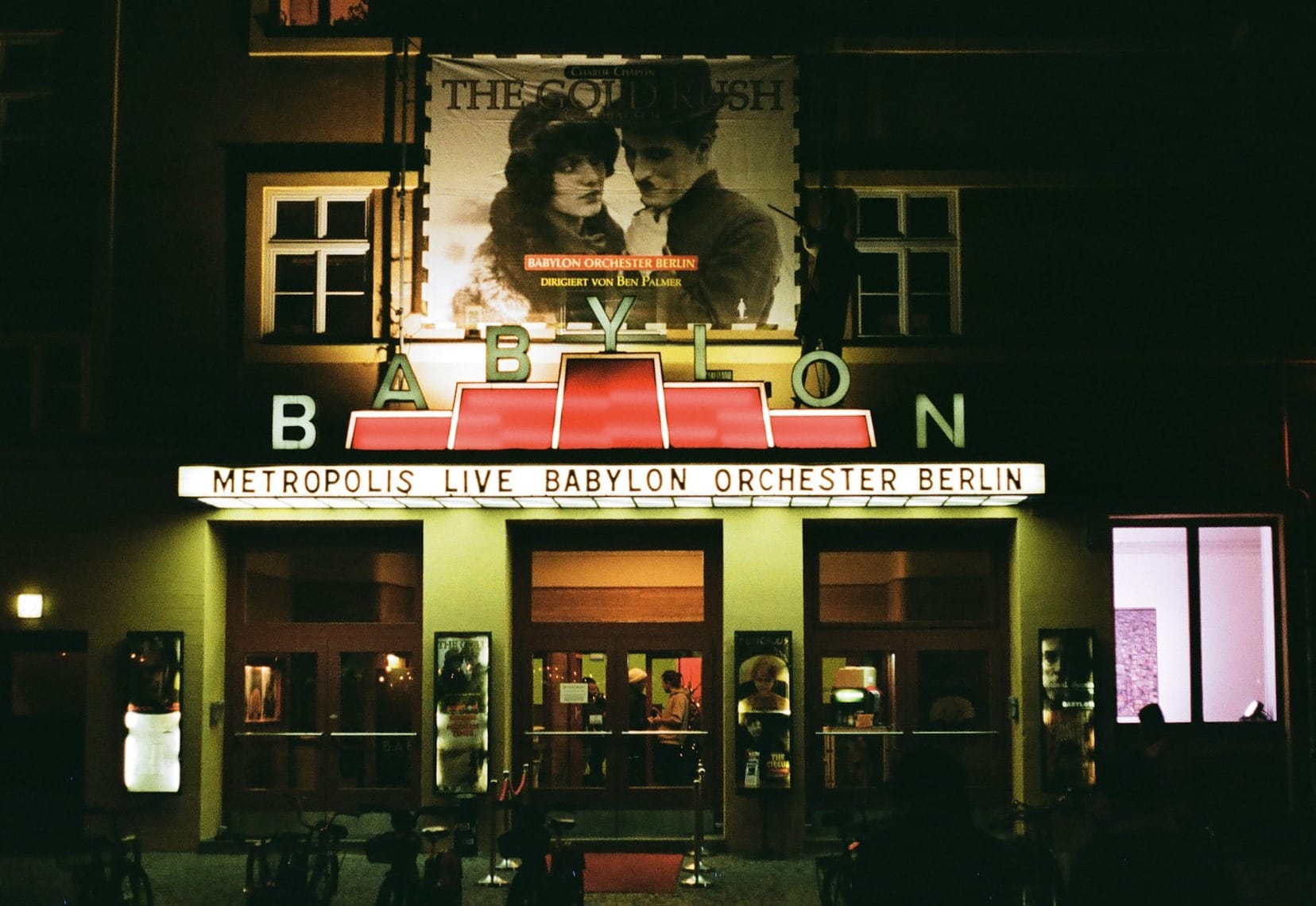 a movie theater at night with people standing outside